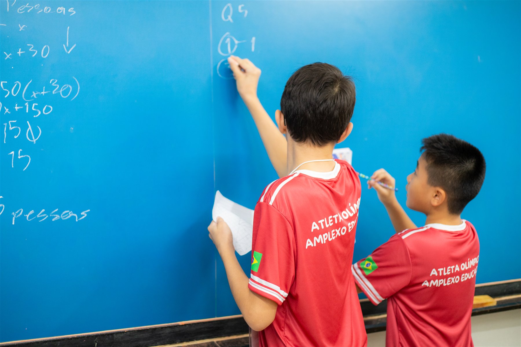 Dois estudantes da Amplexo resolvendo desafios em um quadro